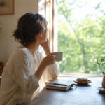 人に合わせて疲れていた女性が朝の光の中で自分の人生を見つめ直している様子